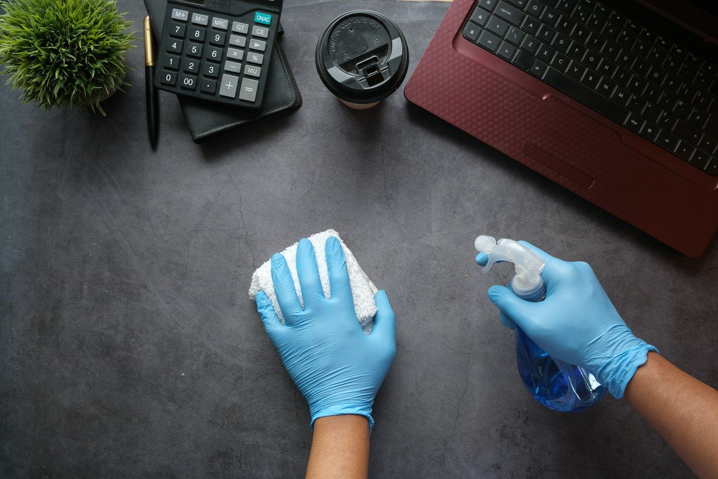 Gloved hands sanitizing an office desk
